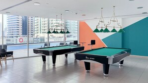 Un espace dédié aux tables de billard, avec deux tables, des chaises et une vue sur le paysage urbain grâce à de grandes fenêtres.