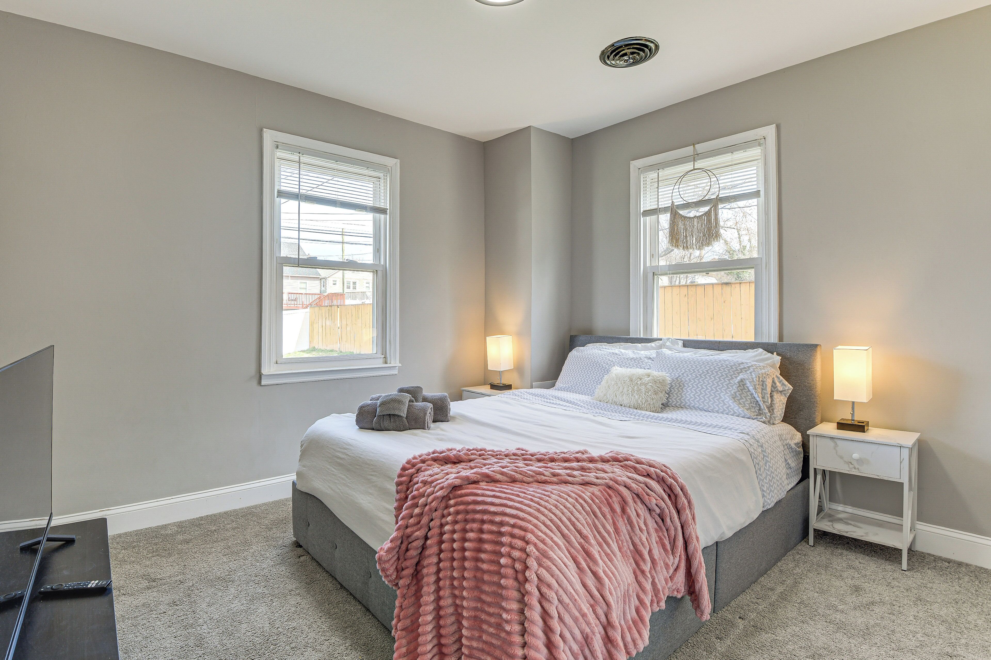 A bedroom with a bed, two bedside lamps, a TV, and a window with blinds.