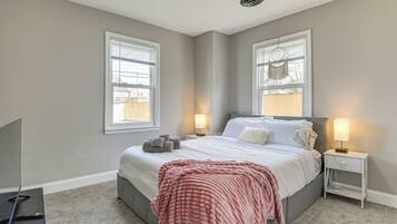 A bedroom with a bed, two bedside lamps, a TV, and a window with blinds.