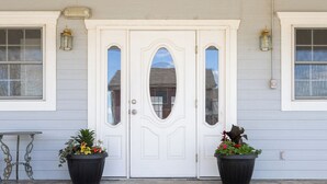 A white double door with glass panels, flanked by two black planters with flowers, and a small table to the left. - Thankers (Wheatland)