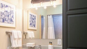 A bathroom with a white sink, a mirror, and a towel rack. There are framed pictures on the wall and a light fixture above the mirror. - Thankers (Wheatland)