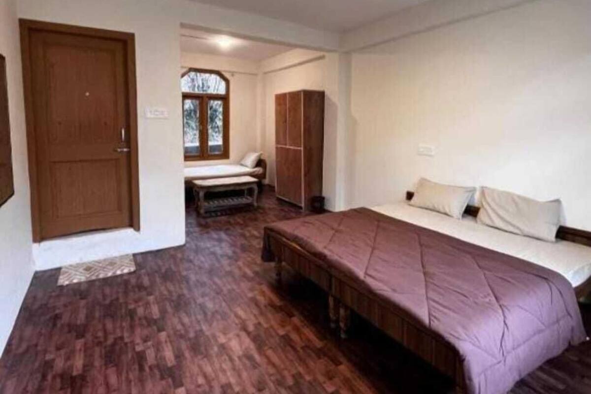 Ein Schlafzimmer mit Holzboden, einem Bett mit violetter Bettdecke, einem Kleiderschrank und einer kleinen Bank.