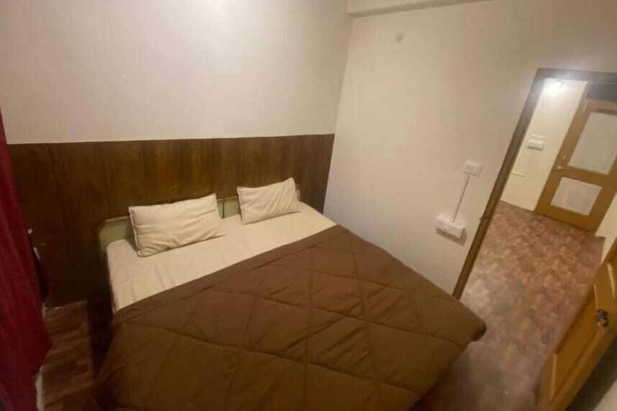Ein Zimmer mit einem Einzelbett, einem Holz-Kopfteil, einer braunen gesteppten Bettdecke und einer weißen Wand.