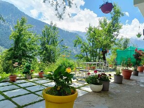 A terrace with potted plants and a table, overlooking a mountainous landscape. - Nomadic Den Manali (Manali)