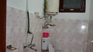 Et lille badeværelse med toilet, håndvask og bruser. To spande, en rød og en sort, står på gulvet.