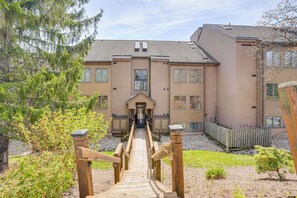 Ein Gebäude mit einem zentralen Eingang, einem hölzernen Weg, der dorthin führt, und einem eingezäunten Gartenbereich.