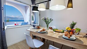 A dining area with a view of the sea, a wooden table set with plates, glasses, and a fruit bowl. - Vila Perla Slatine - Charming 4-bedroom villa with Pool (Slatine)