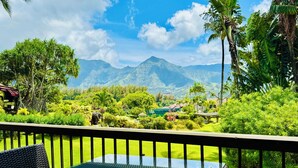Un balcón con una mesa y sillas de vidrio, con vistas a un jardín exuberante y montañas.