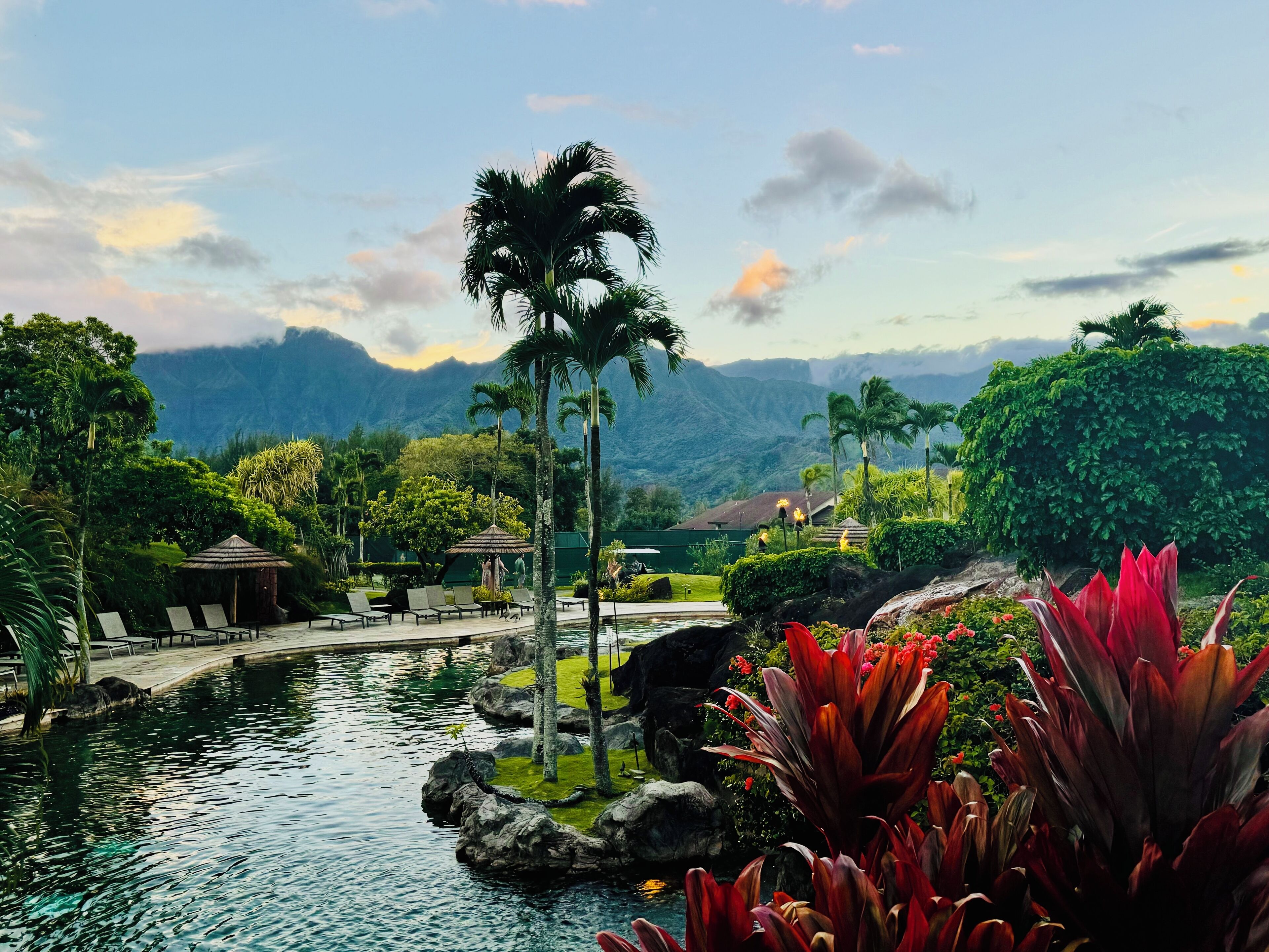 A pool area with lounge chairs, a small pavilion, and a view of mountains in the background.