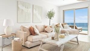 Ein modernes Wohnzimmer mit einem beigen Sofa, einem Couchtisch und Meerblick durch große Fenster.