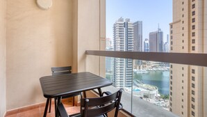 A balcony with a table and chairs, overlooking a marina with high-rise buildings. - Blueground | Jumeirah Beach Residence, pool, nr Marina (Dubai)
