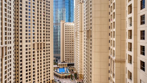 A high-rise building complex with a central courtyard featuring a swimming pool and lounge area. - Blueground | Jumeirah Beach Residence, pool, nr Marina (Dubai)