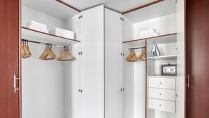 A walk-in closet with wooden hangers, shelves with folded towels, and a safe. - Blueground | Jumeirah Beach Residence, pool, nr Marina (Dubai)