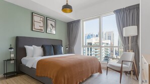 Ein modernes Schlafzimmer mit einem großen Bett, einem Sessel, einem Schreibtisch und Blick auf die Stadt durch das Fenster.