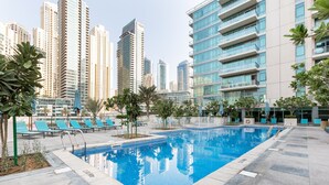 Ein Swimmingpool, umgeben von Liegestühlen und Palmen, mit hohen Gebäuden im Hintergrund.