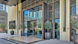 A modern building entrance with glass doors, decorative metal lattice panels, and potted plants.