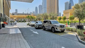 A modern urban street with parked cars, a pedestrian pathway, and tall buildings in the background.