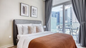 A modern hotel room with a large bed, a balcony with a view of the city, and two framed artworks on the wall.