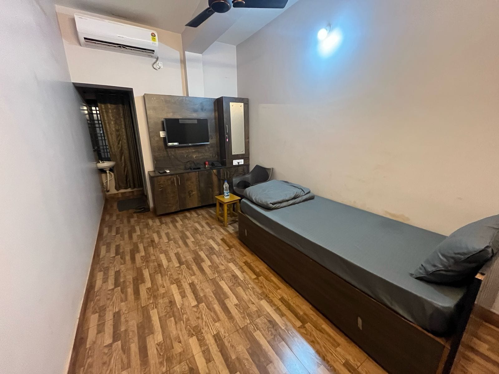 Una habitación pequeña con cama, una mesita, un televisor y un armario.