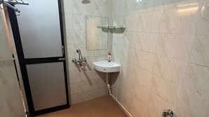 Une petite salle de bain carrelée, équipée d’un lavabo, d’un miroir, d’une douche et de toilettes.
