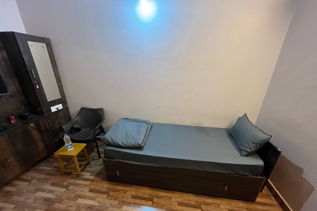 A small, compact room with a single bed, a small table, a chair, and a kitchenette area.