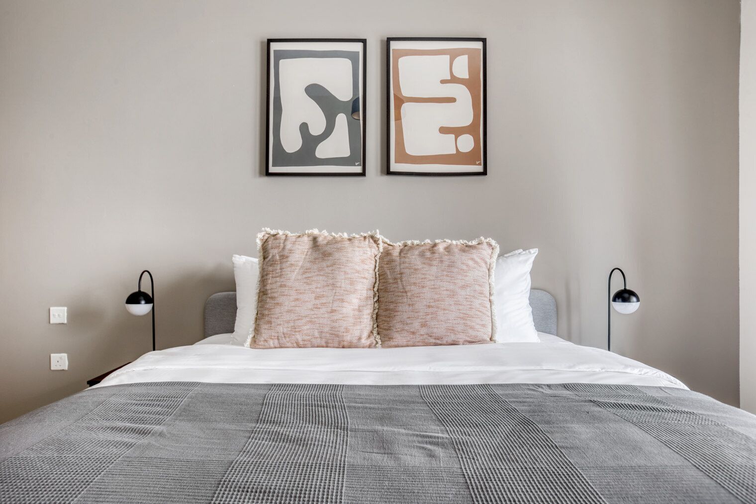 A modern bedroom with a large bed, two wall-mounted abstract art pieces, and two bedside lamps.