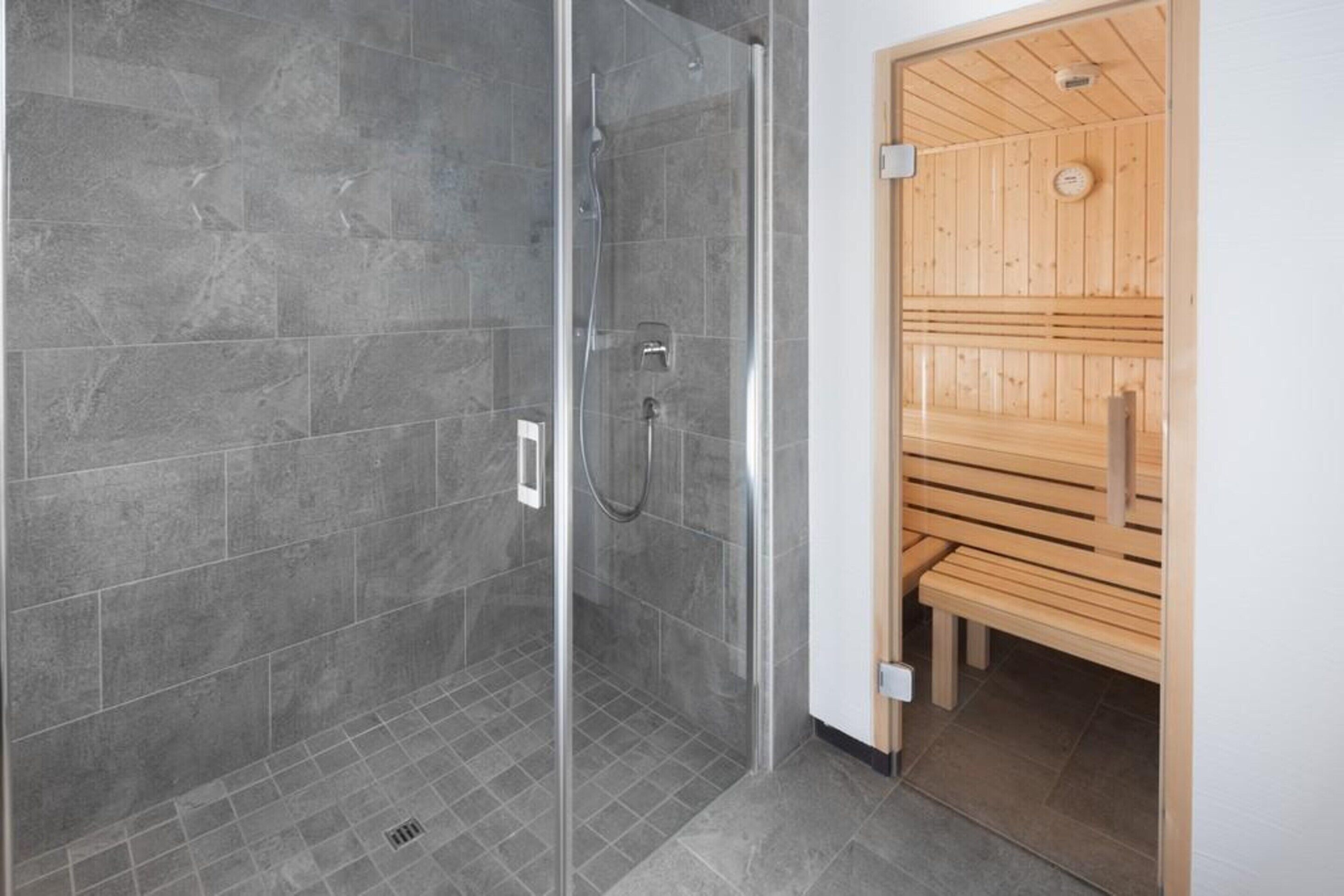 A modern bathroom with a glass shower enclosure and a wooden sauna area.
