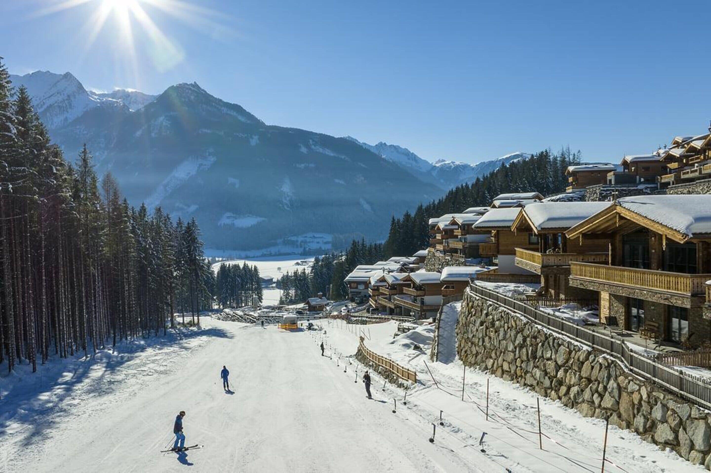 A ski resort with wooden buildings, a snow-covered slope, and mountains in the background.