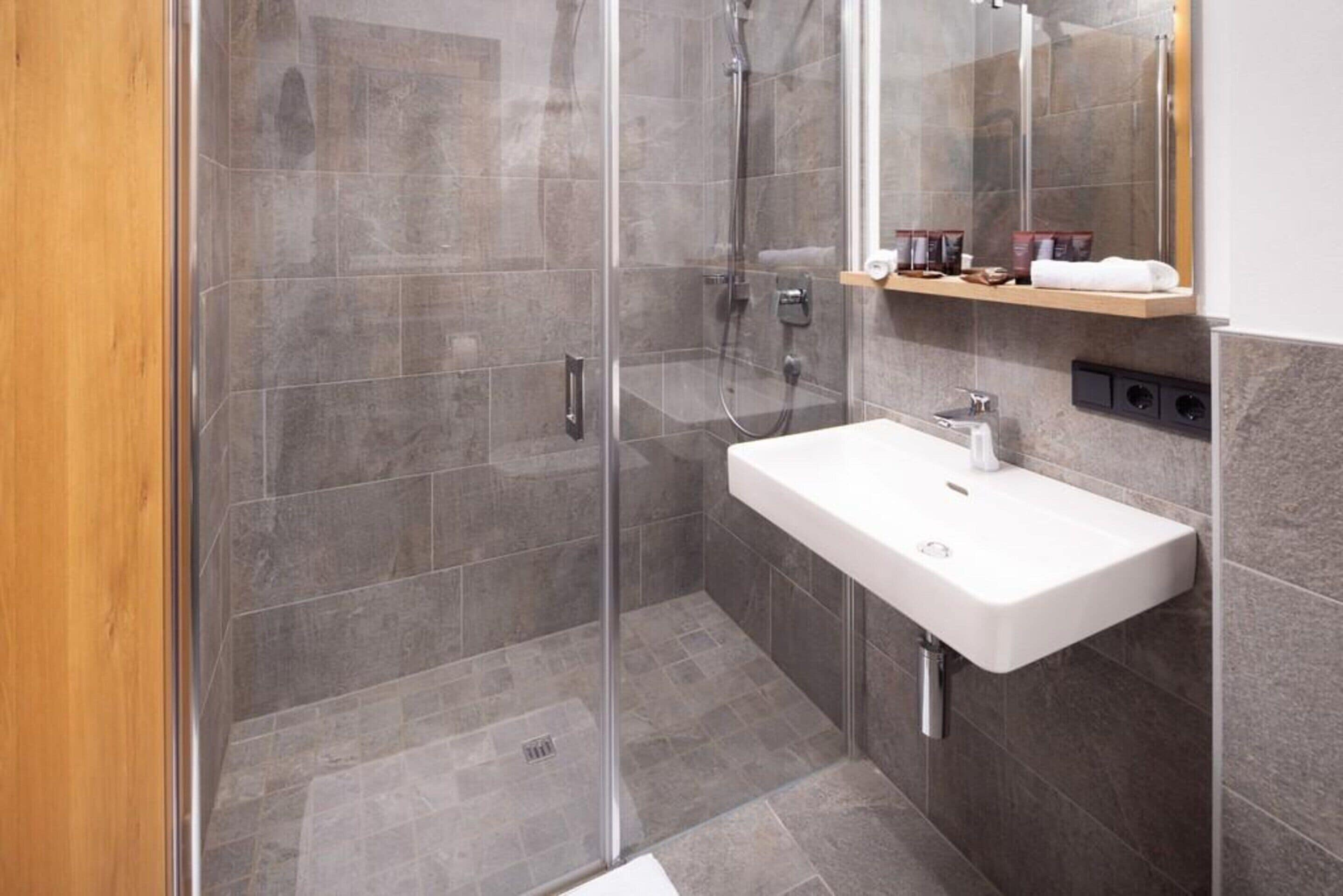 A modern bathroom with a glass-enclosed shower, a white sink, and a mirror above it.