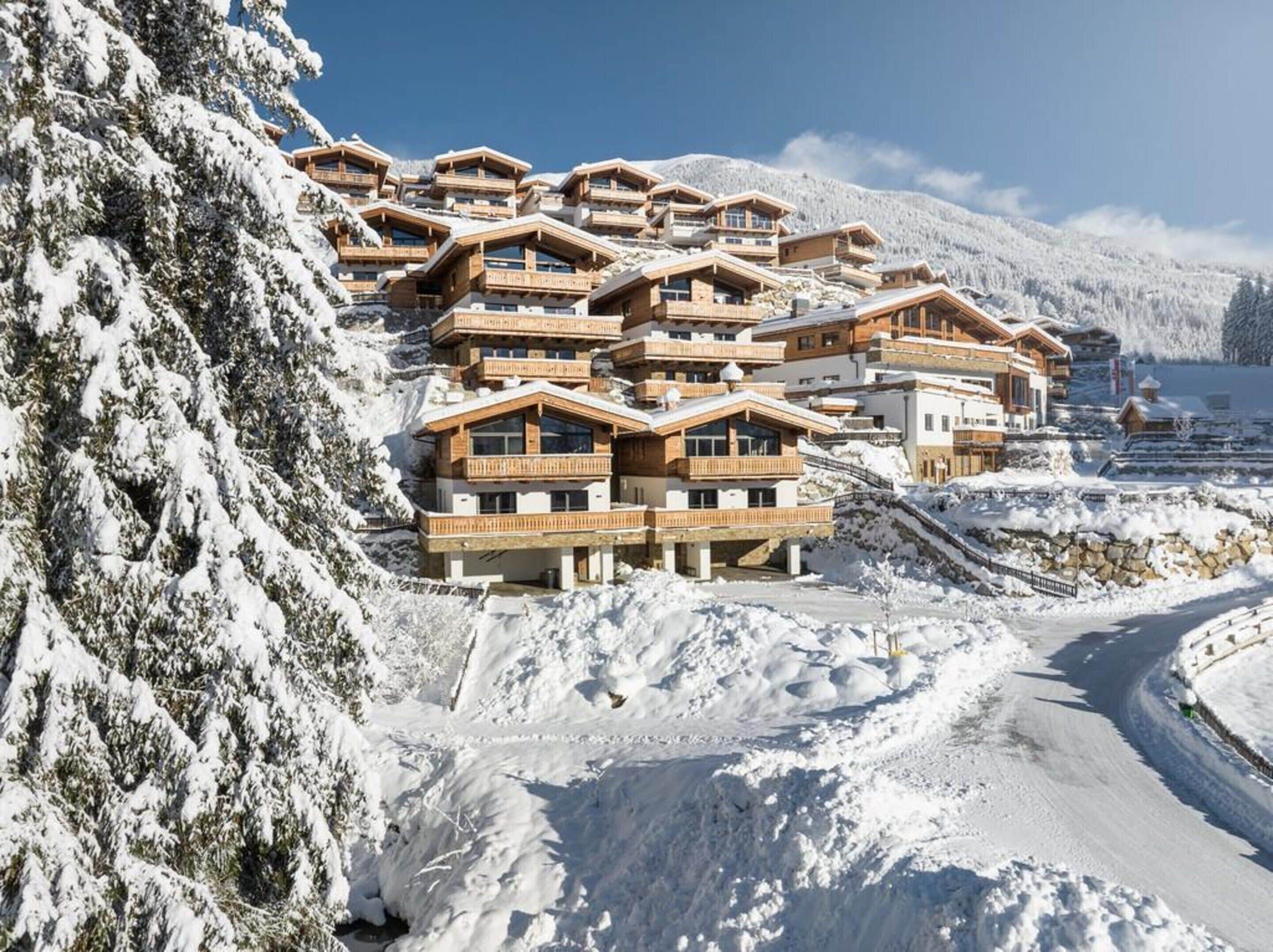 Una località montana innevata con edifici in stile chalet, una strada tortuosa e cielo sereno.