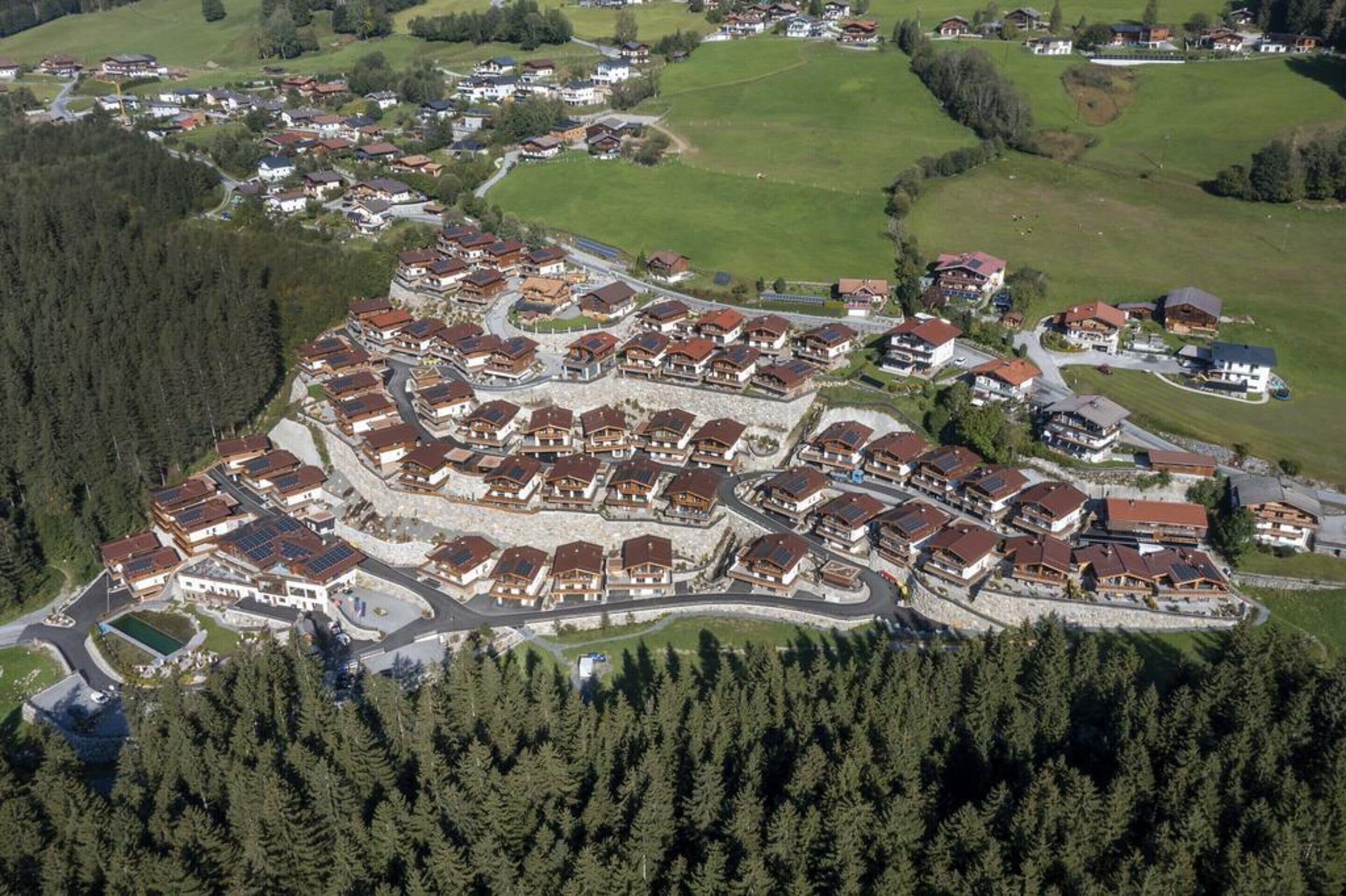 Vista aérea de uma área residencial com casas agrupadas em torno de uma via central, cercada por áreas arborizadas.