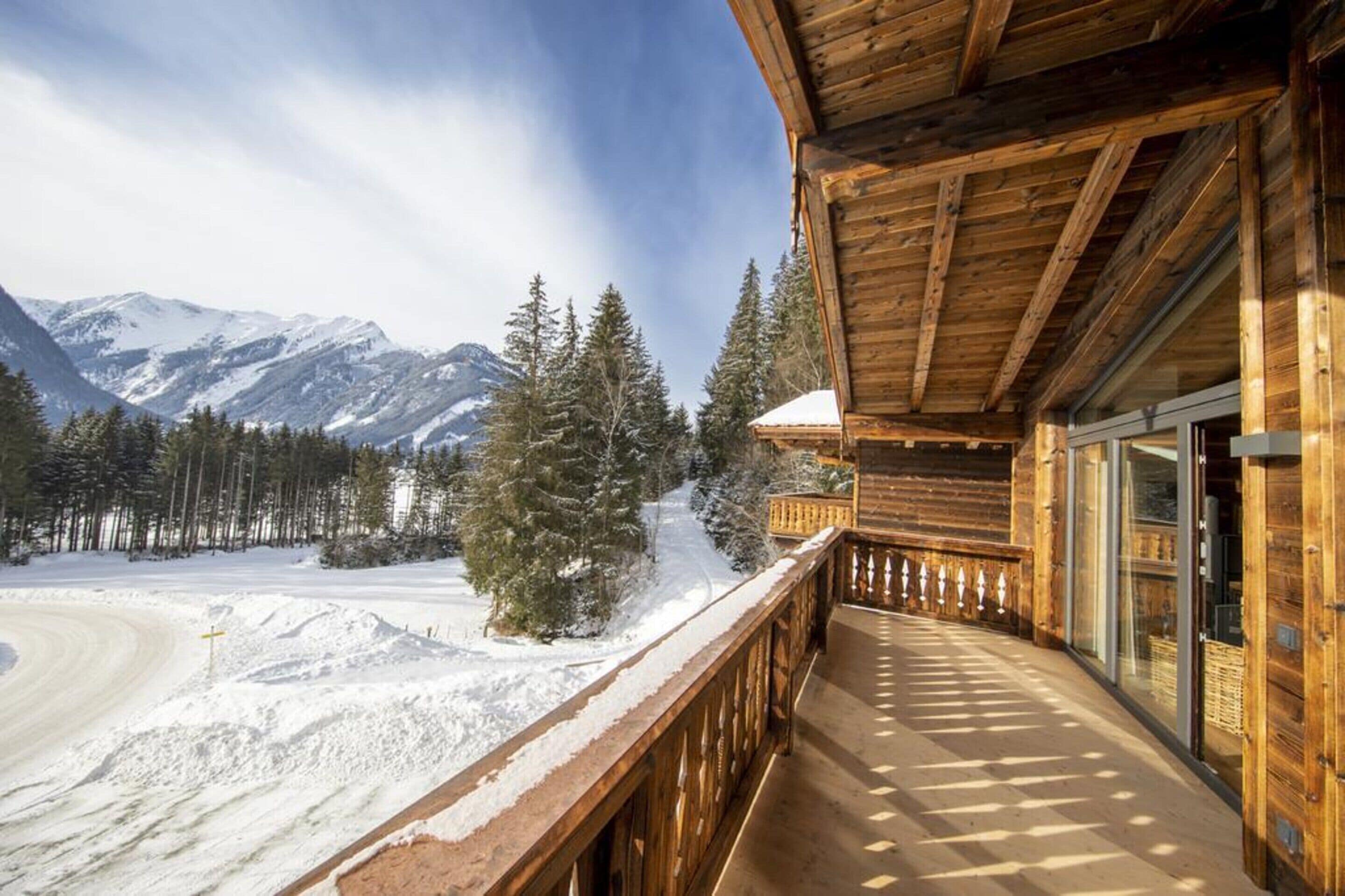 Een houten chalet met een balkon met uitzicht op een besneeuwd berglandschap.