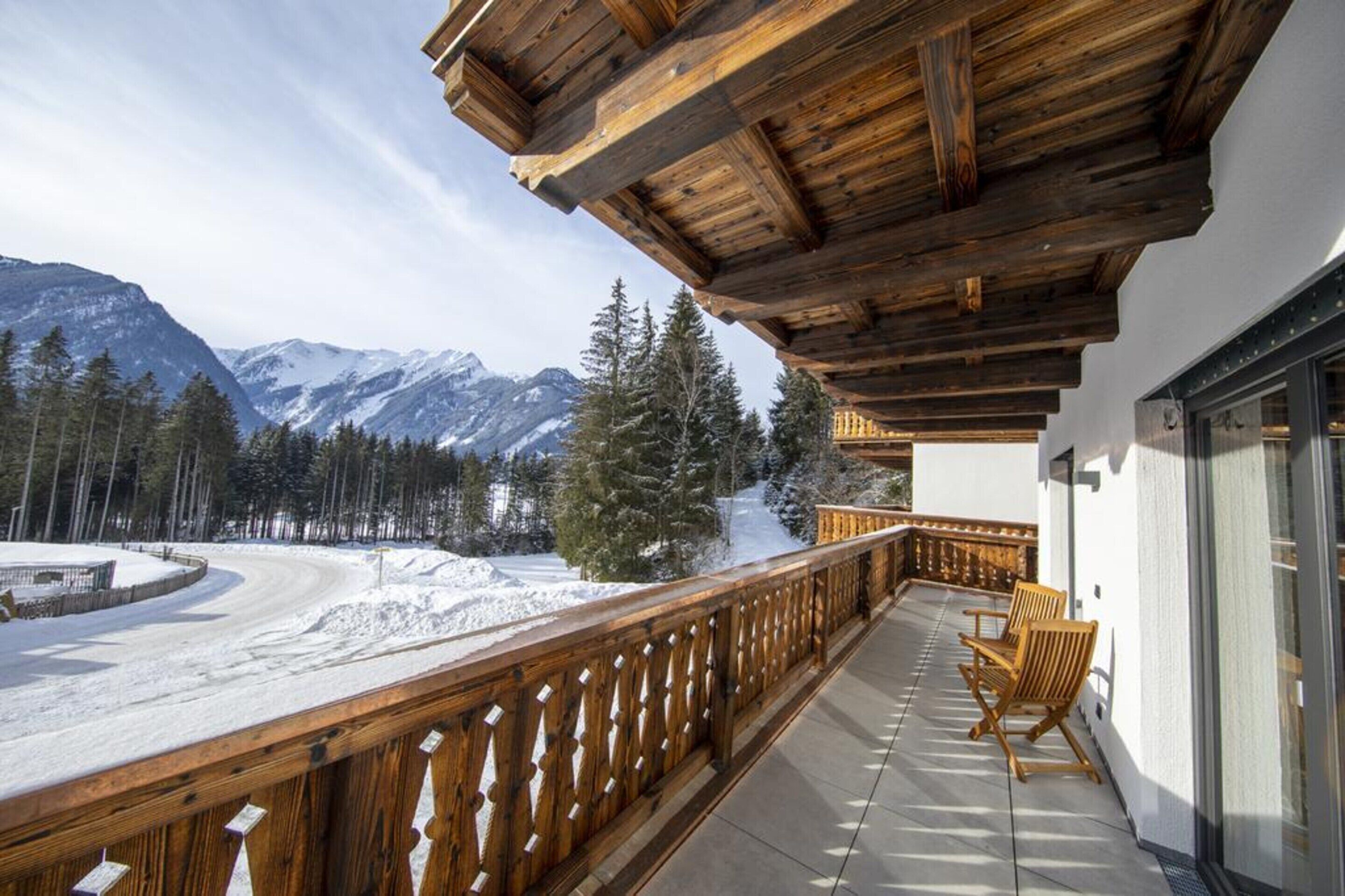 A wooden balcony with a view of snow-covered mountains and pine trees.
