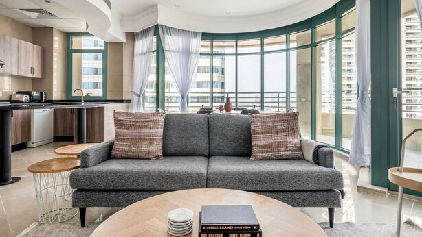Un salon moderne avec un canapé gris, une table basse et une vue sur la ville grâce à de grandes fenêtres.