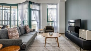 Un salon moderne avec un canapé gris, une table basse ronde, un meuble TV noir et une grande fenêtre avec des rideaux.