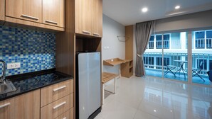 Cozinha moderna com armários de madeira, bancada preta e geladeira embutida. Há uma pequena mesa de madeira e uma cadeira perto de uma grande janela com vista para o exterior.