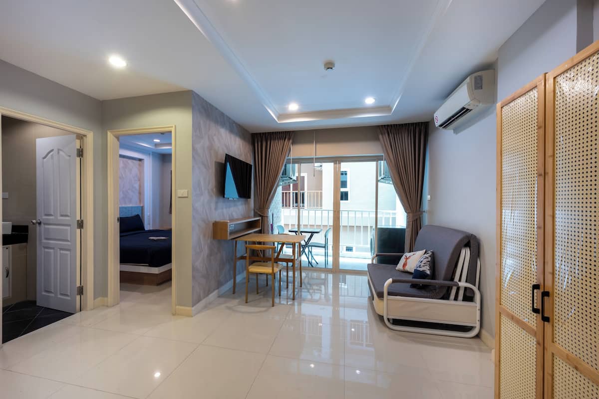 A modern hotel room with a bed, a sofa, a dining table, and a balcony with a view.