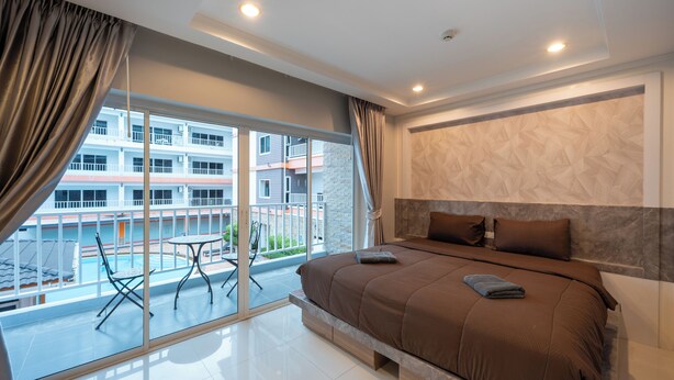 Quarto com uma cama grande, vista para uma piscina e varanda com mesa e cadeiras.