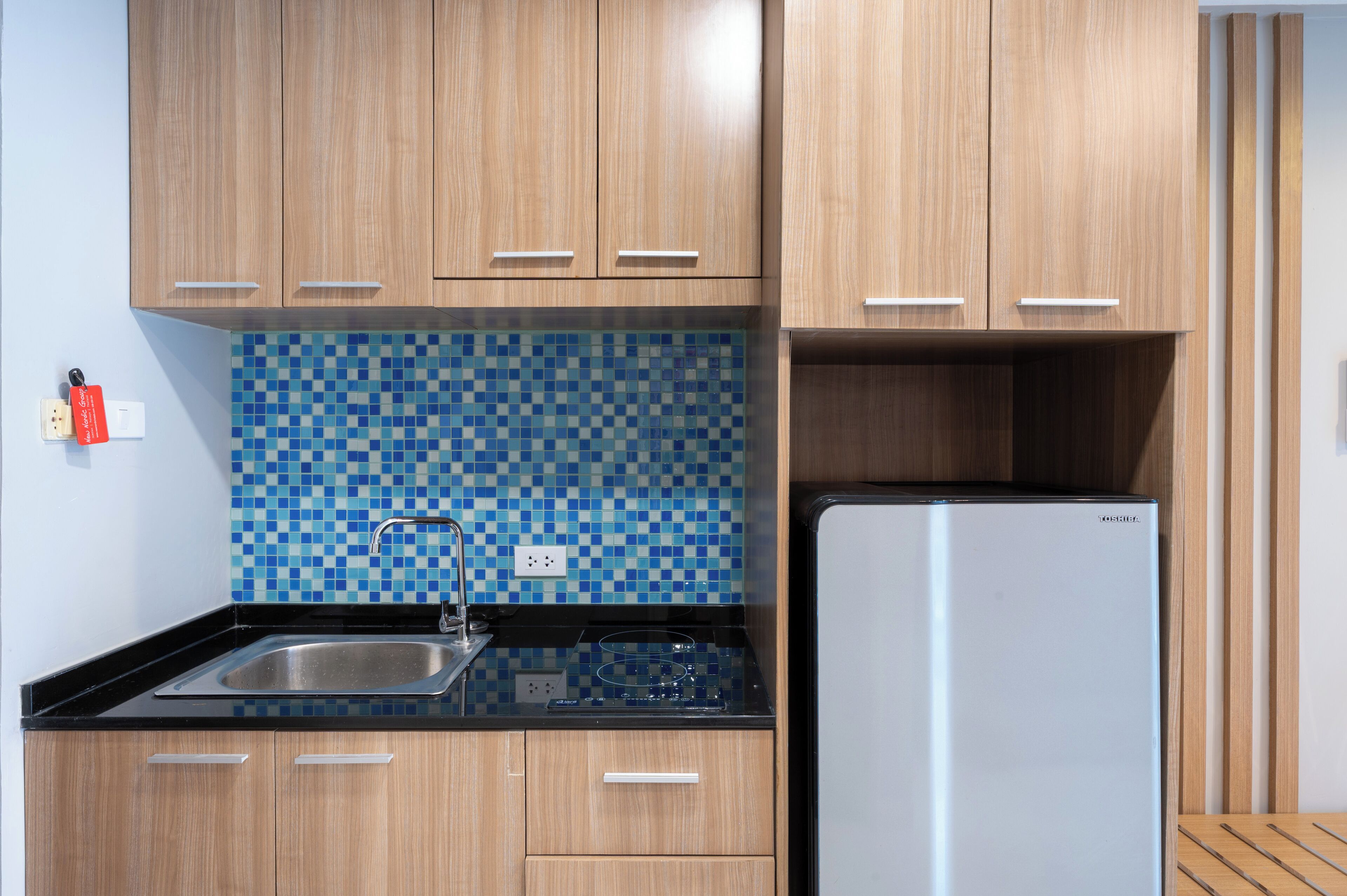 A kitchen with wooden cabinets, a blue mosaic backsplash, a stainless steel sink, and a built-in refrigerator.