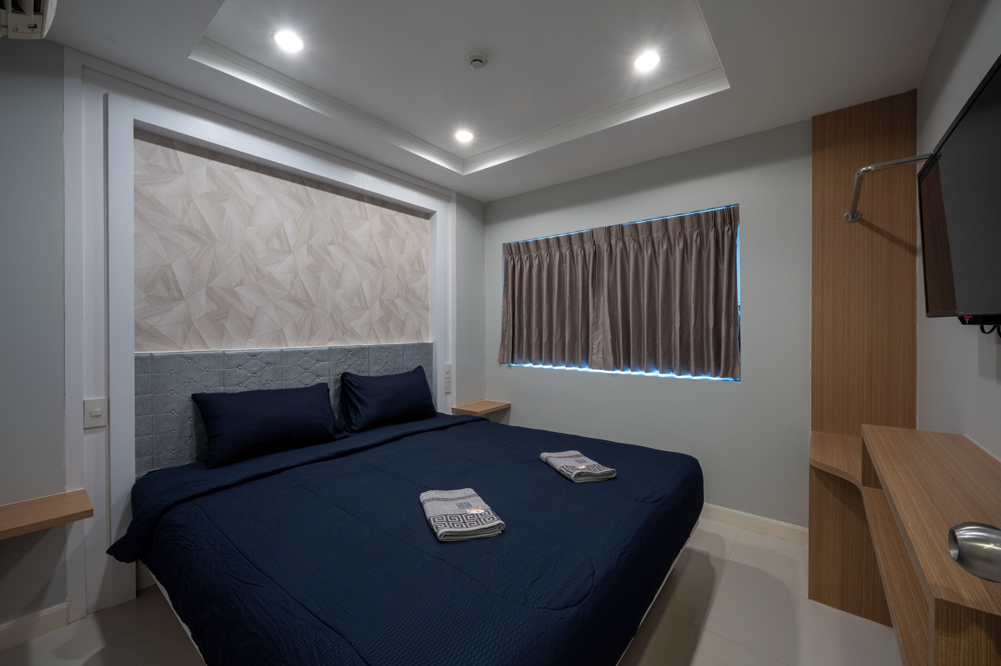 A modern bedroom with a large bed, a TV, and a window with curtains.