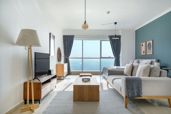 A modern living room with a large window, a flat-screen TV, a sofa, a coffee table, and a floor lamp.