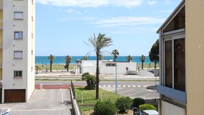A view of a building with a balcony overlooking a street with palm trees and a clear blue sky. - St Cyprien beautiful cozy apartment sea view (Saint-Cyprien)