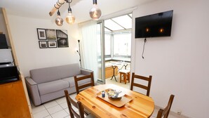 A modern living space with a sofa, dining table, and chairs, a TV mounted on the wall, and a large window providing natural light. - St Cyprien beautiful cozy apartment sea view (Saint-Cyprien)