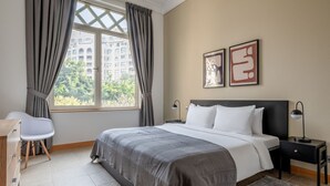 Un dormitorio con cama, escritorio, silla, ventana con cortinas y dos cuadros en la pared.