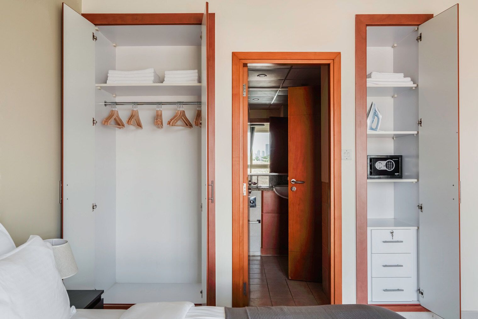 A hotel room with a walk-in closet, a bed, a nightstand, and a view of the city through the window.