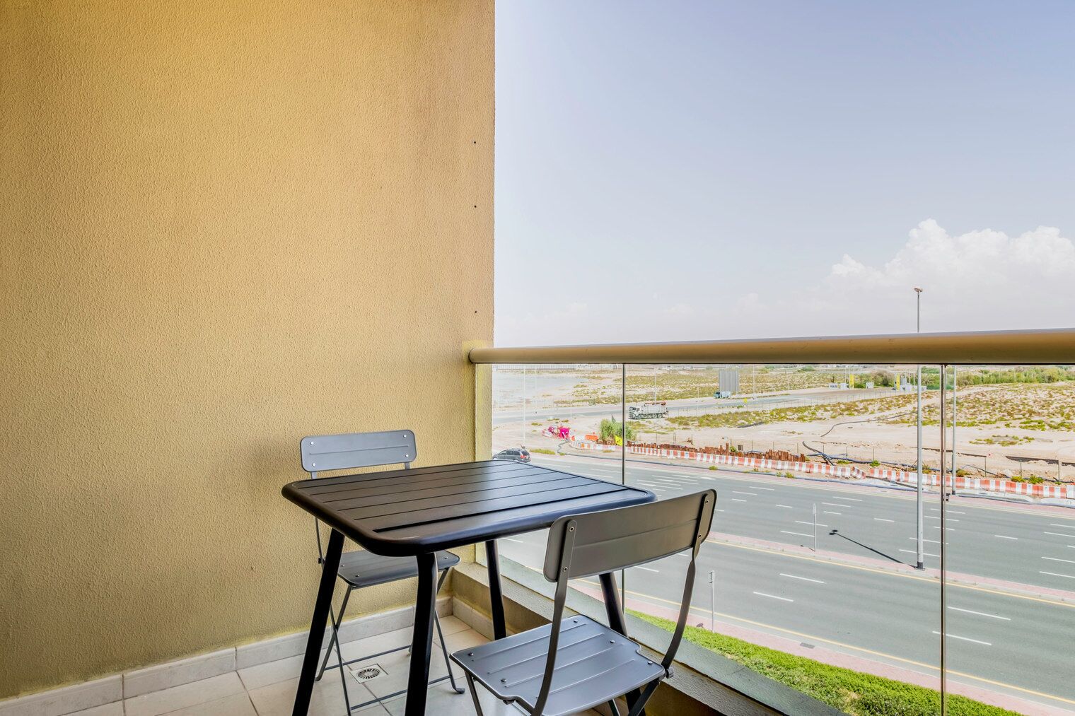 Ein Balkon mit Tisch und Stühlen, der einen Blick auf eine Straße und eine Baustelle bietet.