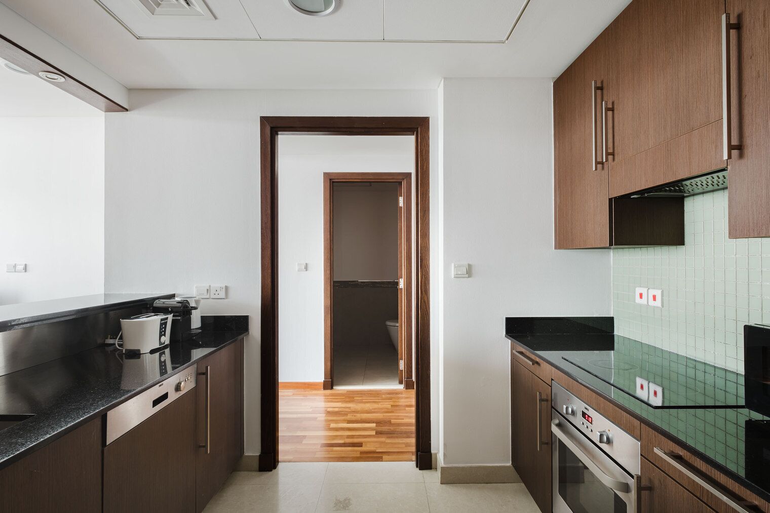 A modern kitchen with dark wooden cabinets, a black countertop, and a green tiled backsplash.
