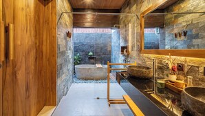 A modern bathroom with stone walls, wooden accents, and a large mirror.