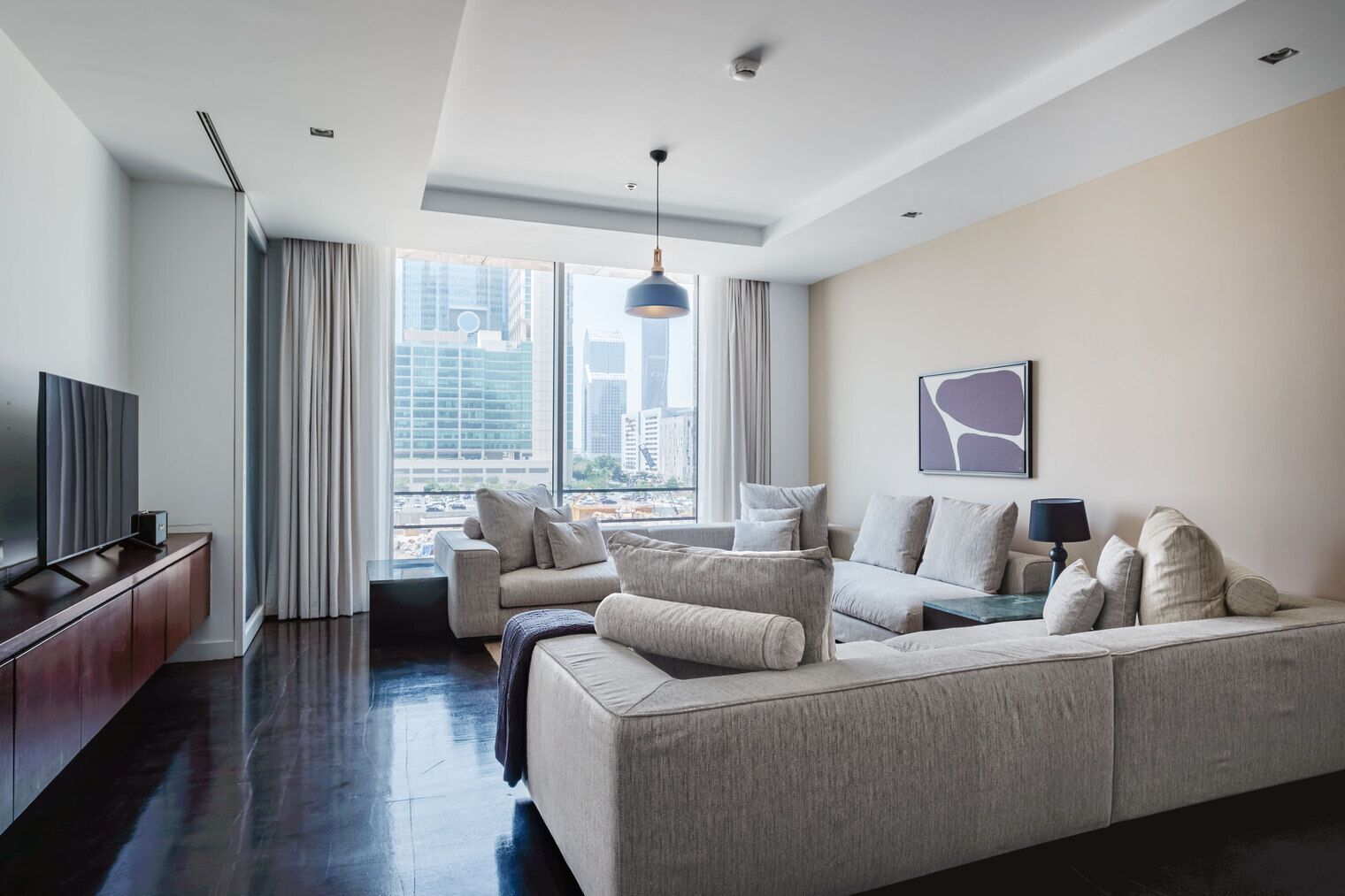 Ein modernes Wohnzimmer mit einer großen Couch, einem Fernseher und Blick auf die Stadt durch große Fenster.