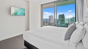 Habitación de hotel con una cama grande, televisión en la pared y vistas a la ciudad a través de un ventanal amplio.